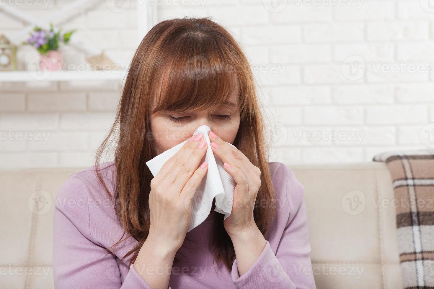 Sick woman sitting at home with high fever. Cold, flu, fever and migraine, sneeze. Copy space. Runny nose photo