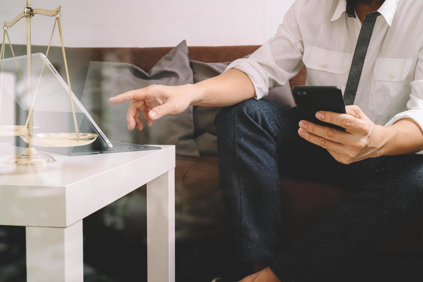 Justice and Law context.Male lawyer hand sitting on sofa and working with smart phone,digital tablet computer docking keyboard with gavel and document on living table at home,filter effect photo