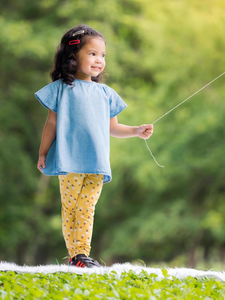 niña asiática parada en la alfombra, jugando y aprendiendo fuera de la escuela para disfrutar en el parque natural foto