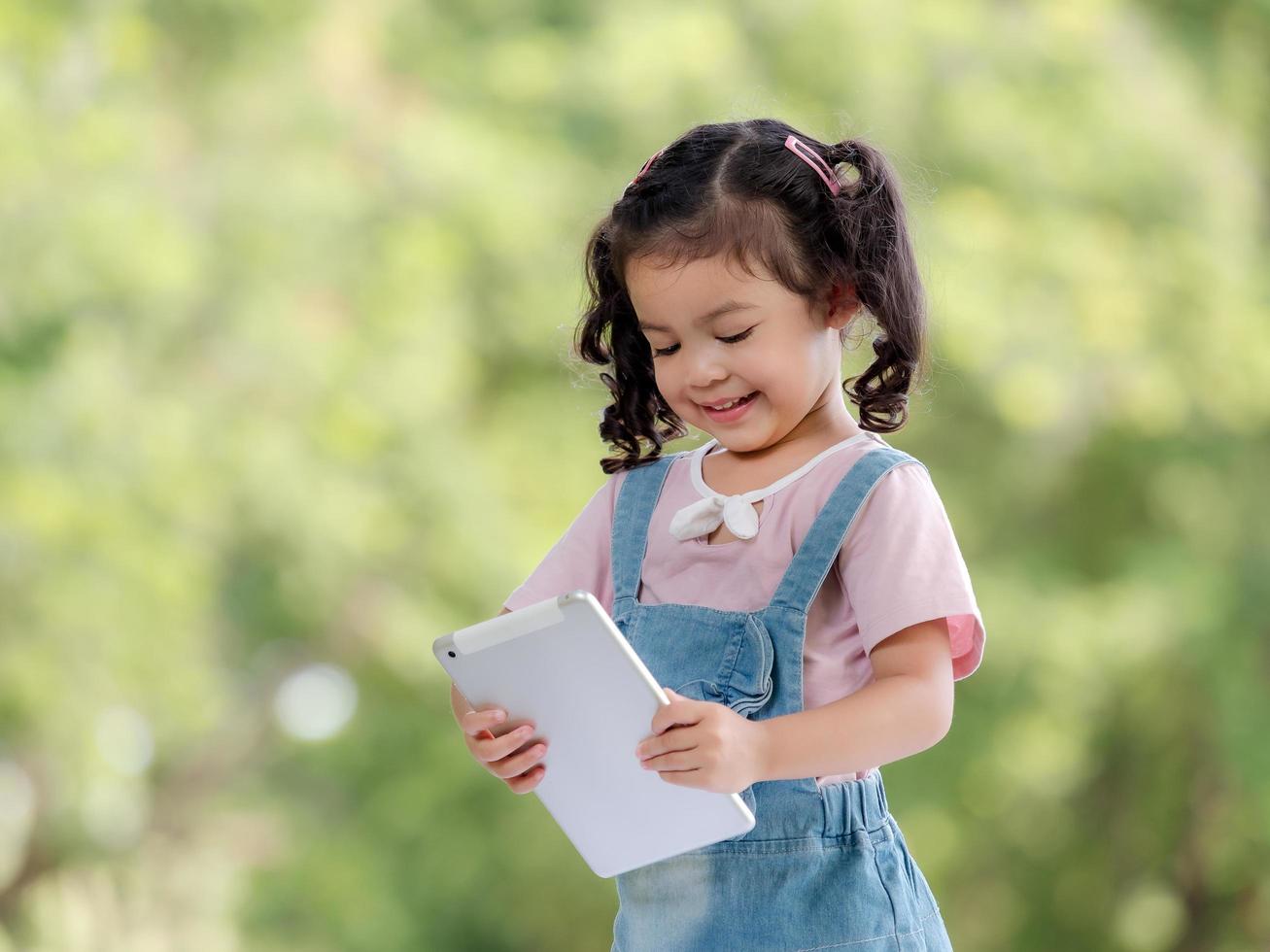 A cute Asian girl is using a tablet for fun playing games and learning outside of school in the park photo