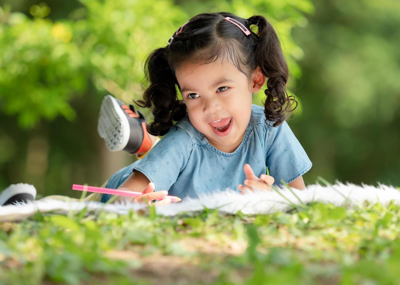 An Asian girl is lying on the carpet and painted with crayons, Which is fun learning outside the school in the nature park photo