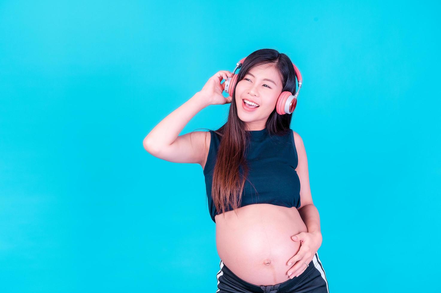 Asian beautiful pregnant woman stands relaxed and enjoys listening to music on headphones connected to the internet photo