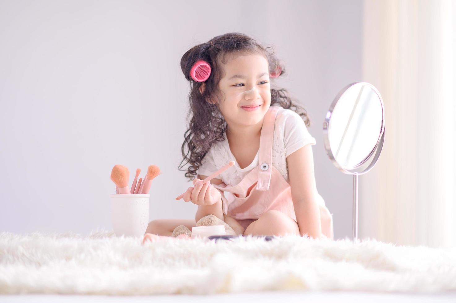 una linda niña asiática está felizmente aplicando pinceles de maquillaje con polvo en su dormitorio foto