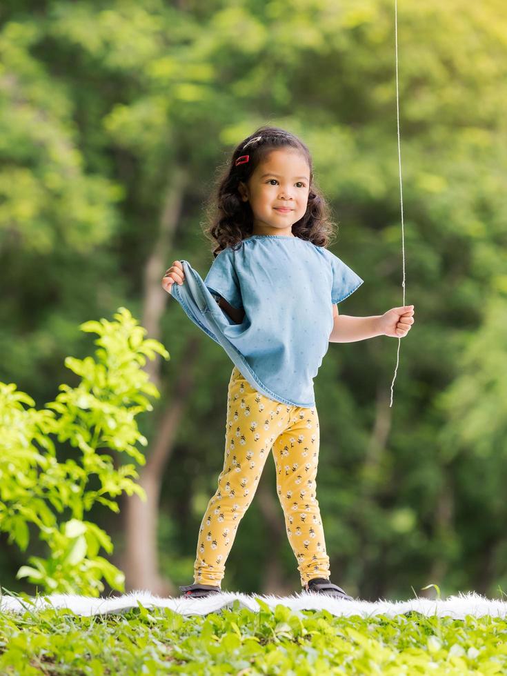 niña asiática parada en la alfombra, jugando y aprendiendo fuera de la escuela para disfrutar en el parque natural foto