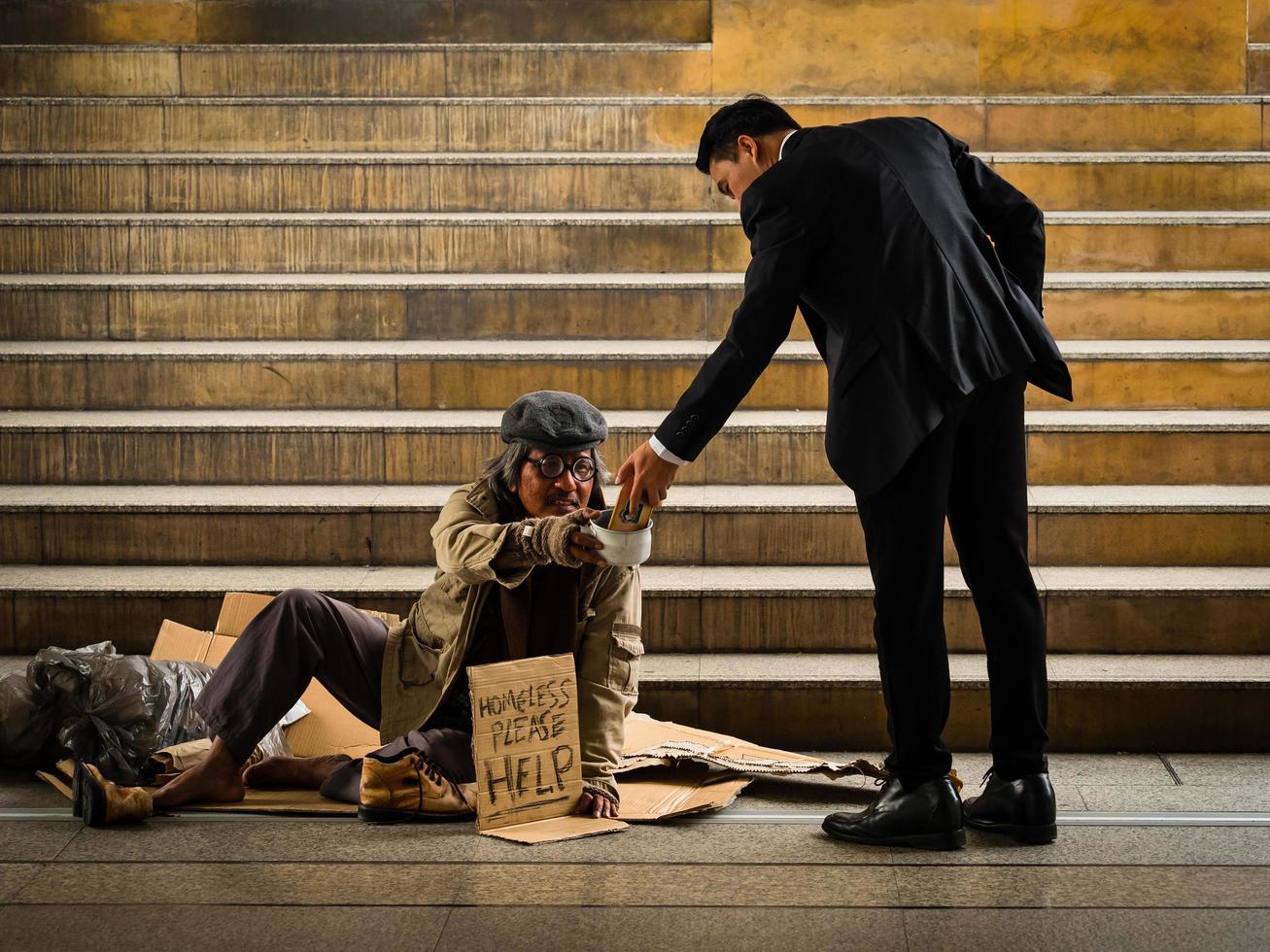 A businessman gives smartphone to a homeless man sitting on a ladder photo