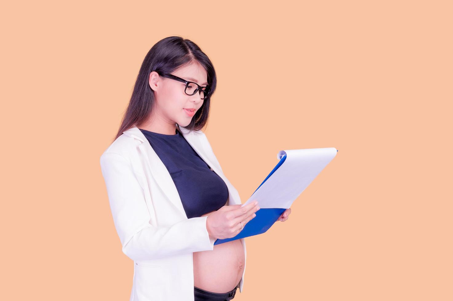 una hermosa mujer asiática embarazada sosteniendo una carpeta de papel, relajándose y disfrutando de su trabajo foto