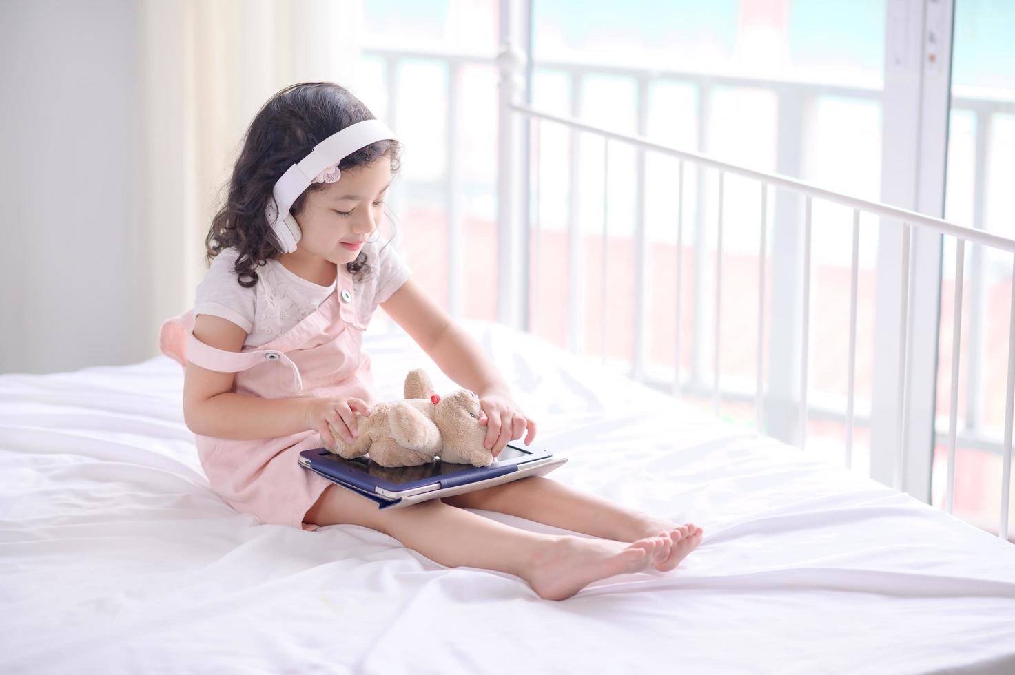 A cute Asian girl is using a tablet for fun playing games and learning  in the room photo