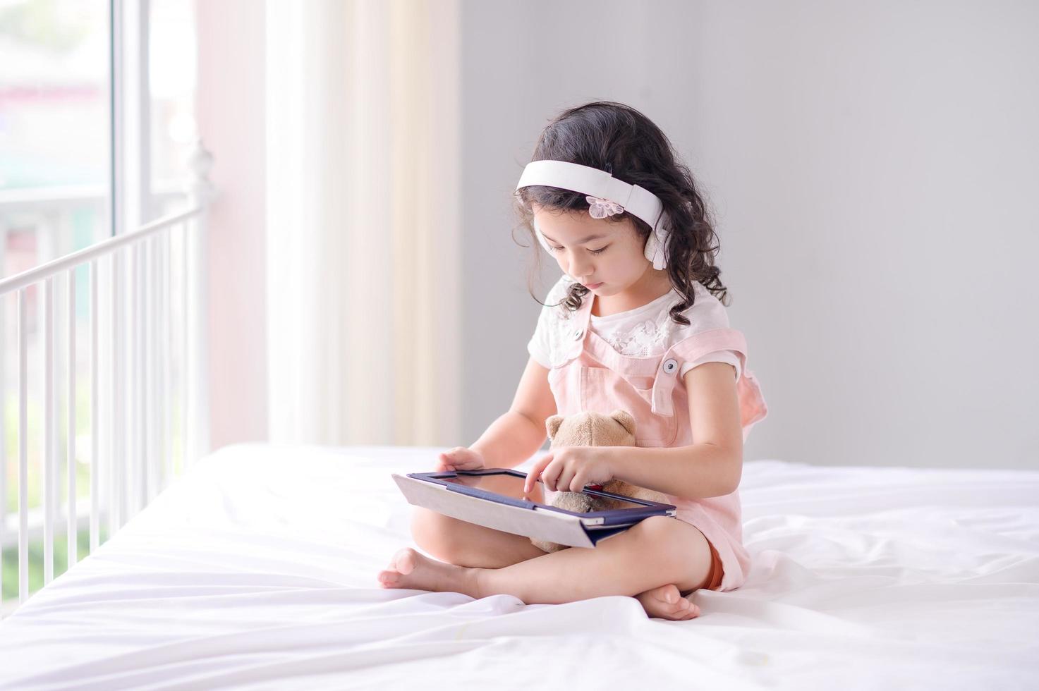 una linda chica asiática está usando una tableta para divertirse jugando y aprendiendo en la habitación foto