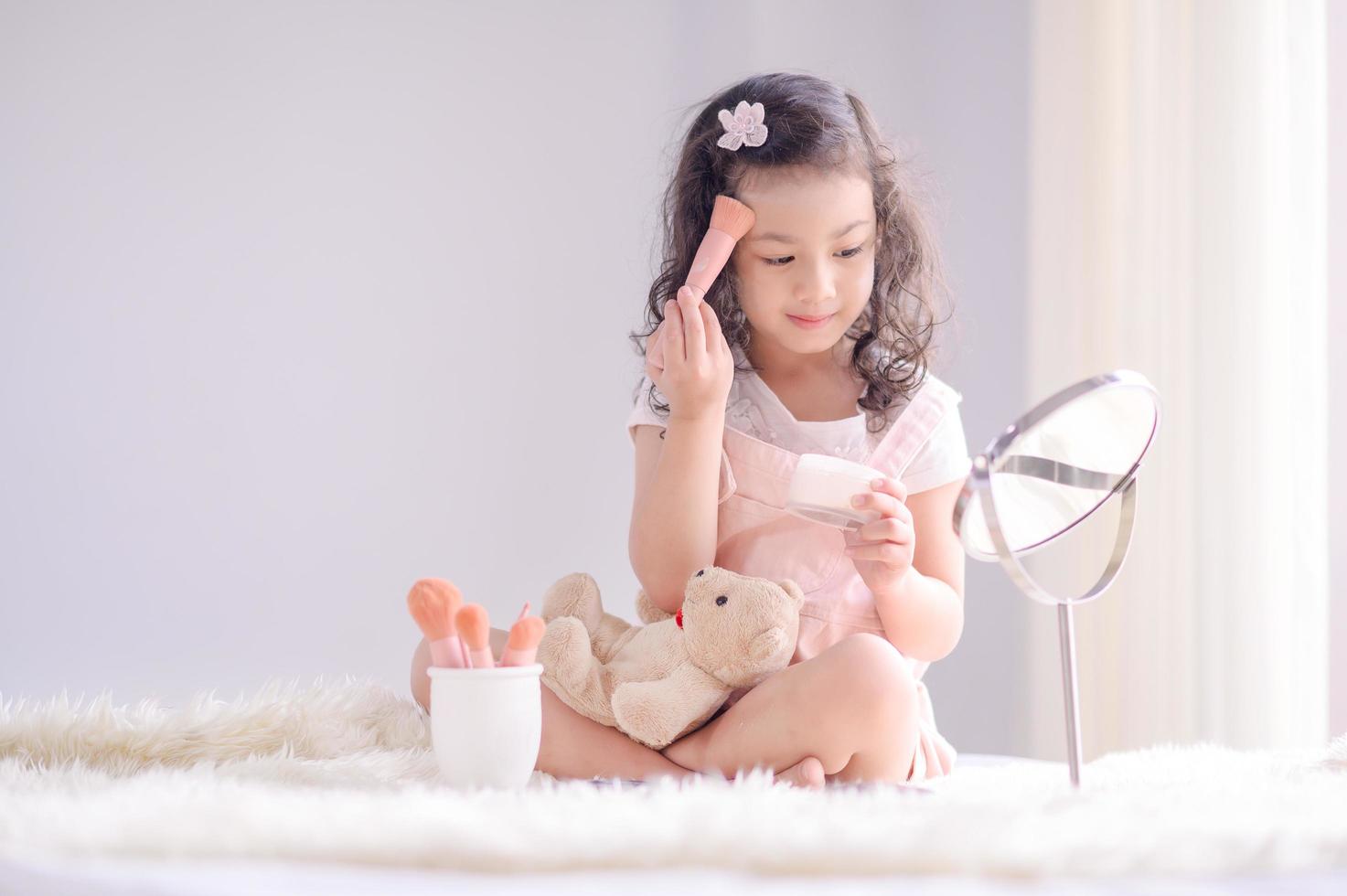 A cute little Asian girl is happily applying makeup brushes with powder in her bedroom photo