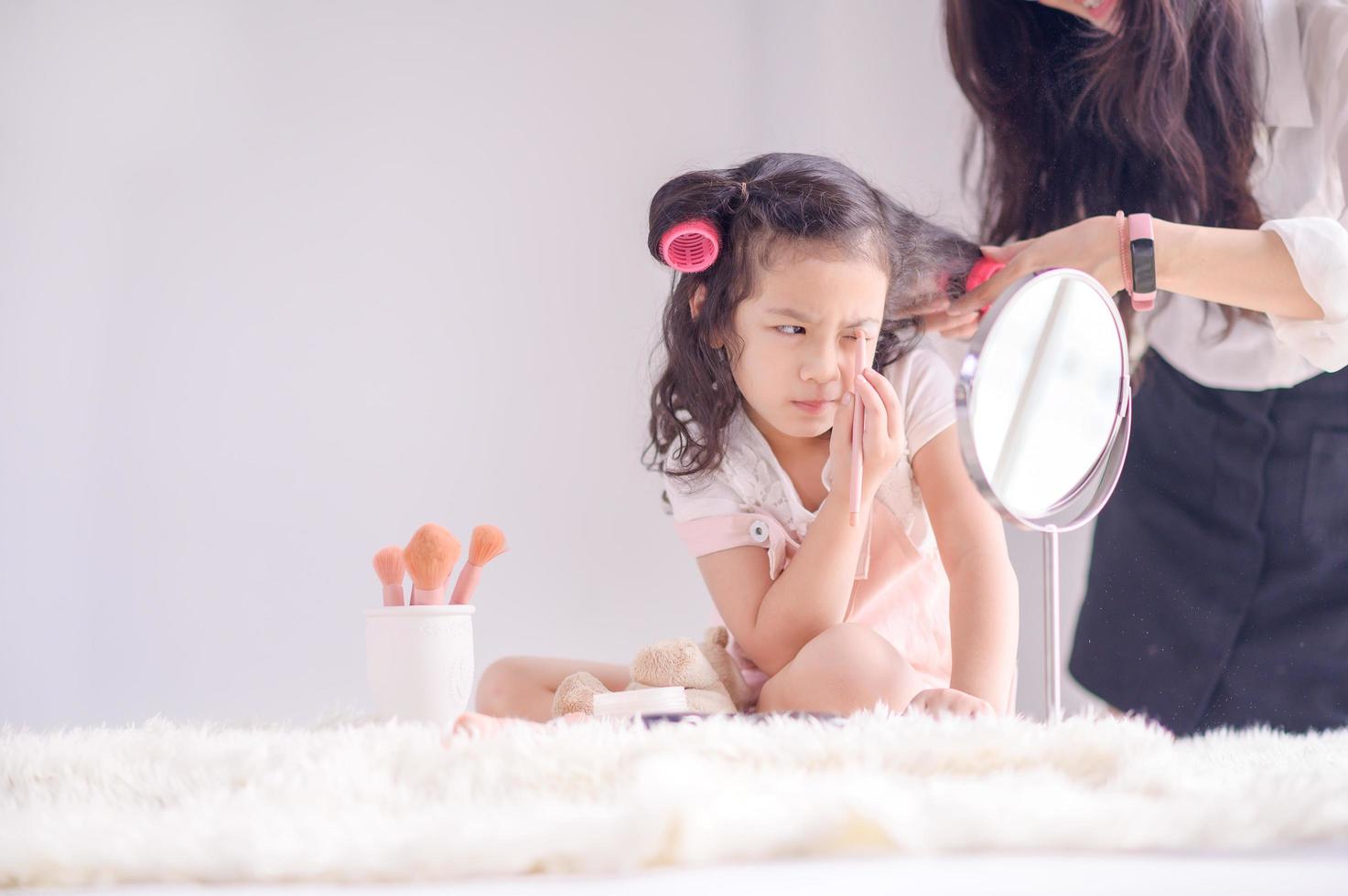 una linda chica asiática se divierte aplicando polvo de maquillaje en su dormitorio mientras la esteticista se peina foto