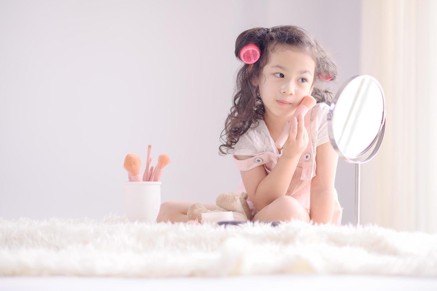 una linda niña asiática está felizmente aplicando pinceles de maquillaje con polvo en su dormitorio foto