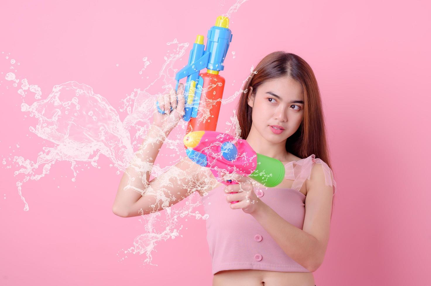 A beautiful Asian woman shows a gesture while holding a plastic water gun during the Songkran festival photo