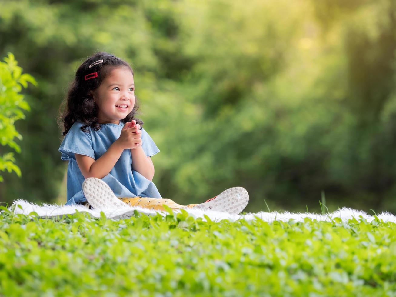 niña asiática sentada en la alfombra, relajándose y aprendiendo fuera de la escuela para disfrutar en el parque natural foto