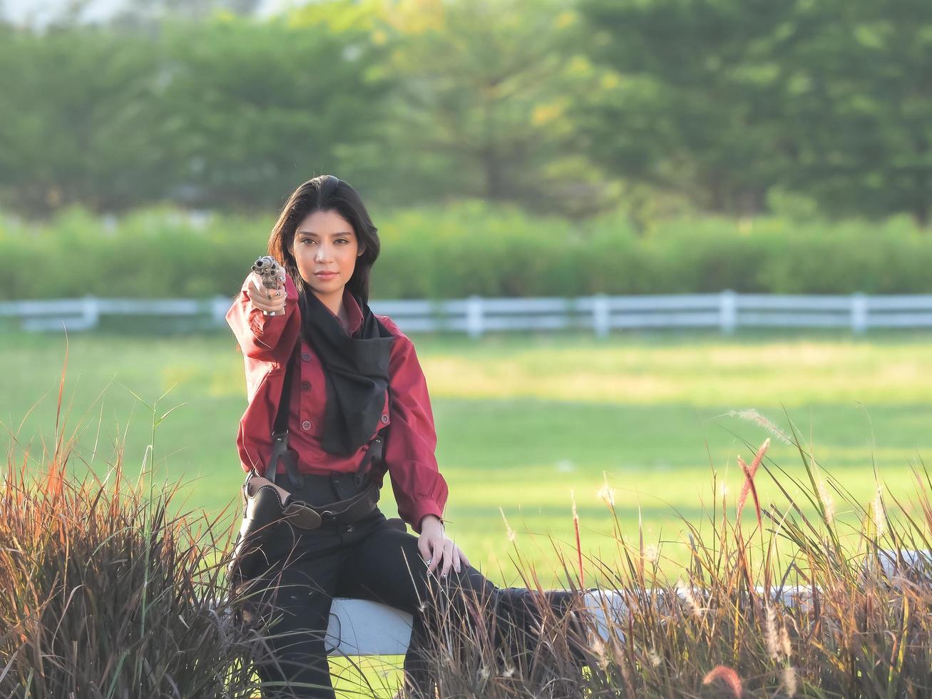 A beautiful western cowgirl sits on a fence and points to a self defense gun while working on the farm photo