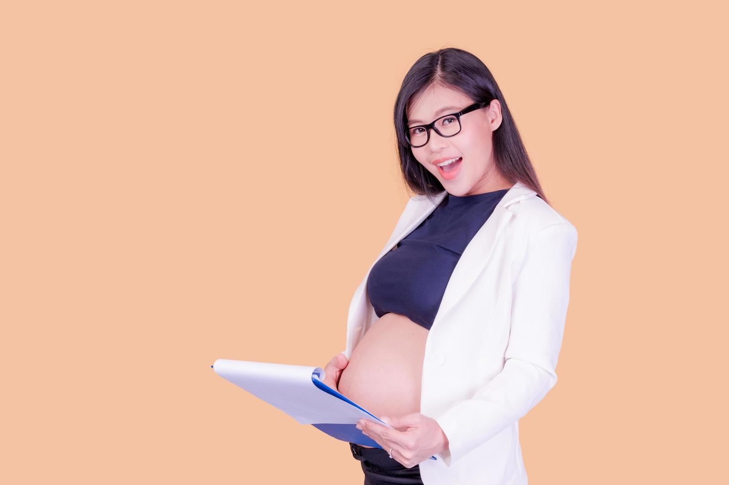 A beautiful pregnant Asian woman holding a paper binder, relaxing and enjoying her work photo