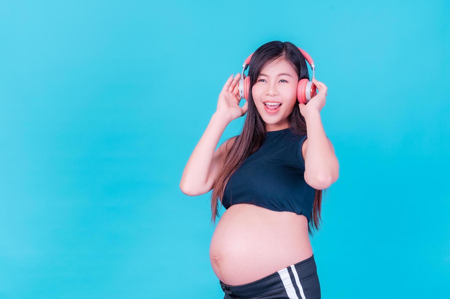 hermosa mujer asiática embarazada se relaja y disfruta escuchando música en auriculares conectados a Internet foto