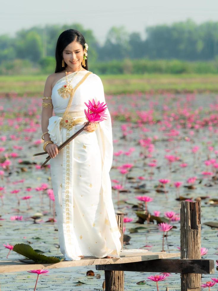 una elegante mujer tailandesa con ropa tradicional tailandesa que lleva flores de loto recolectadas en un campo de loto foto