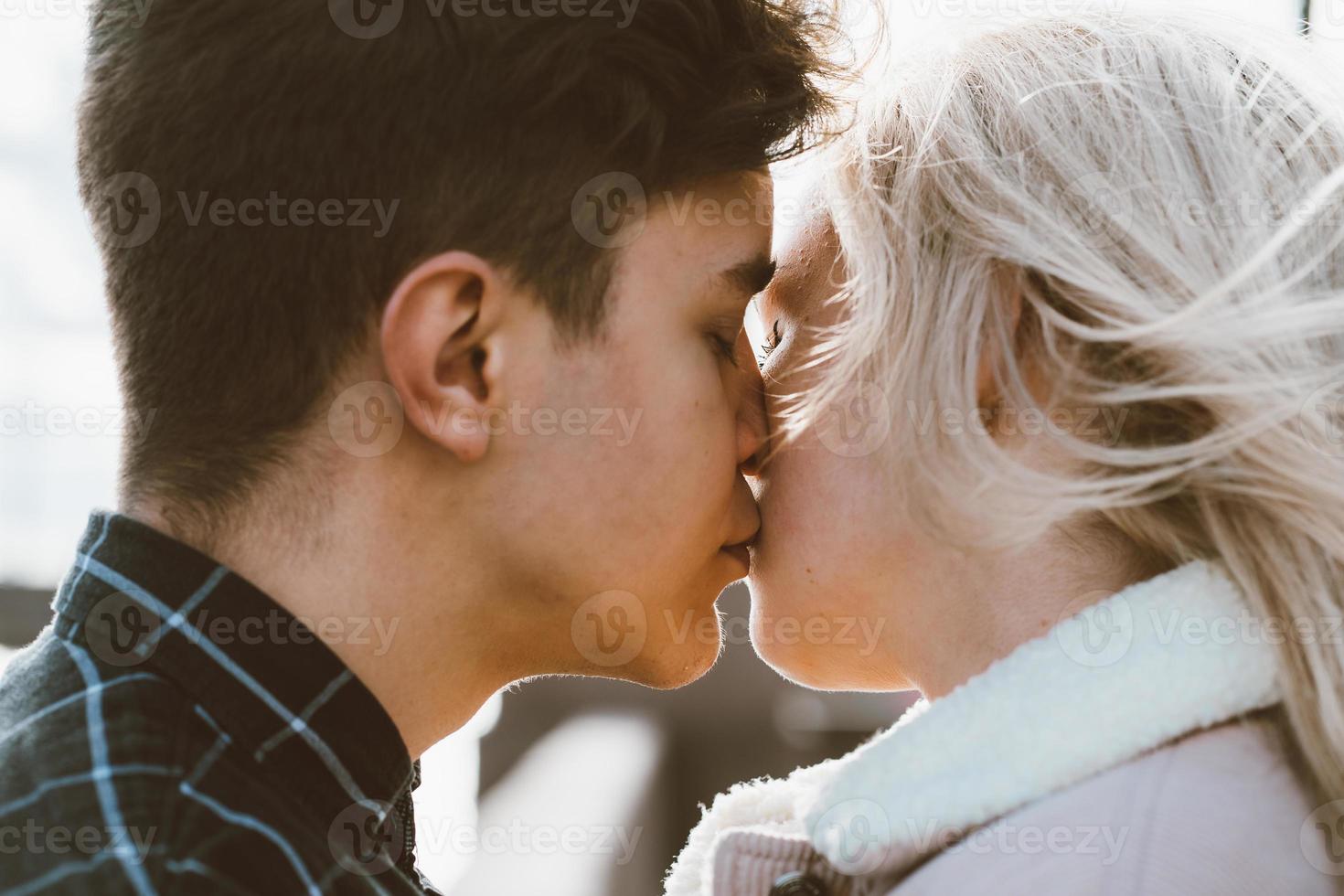 The boy looks tenderly at girl and wants to kiss. A young couple stands embracing. The concept of teenage love and first kiss, sincere feelings of man and woman. The city, the waterfront. Close up photo