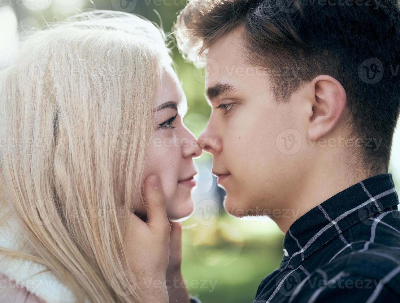 un hombre llama cariñosamente mira a la mujer, el chico y la chica valen cerca, tocándose las puntas de las narices. concepto de amor adolescente y primer beso foto