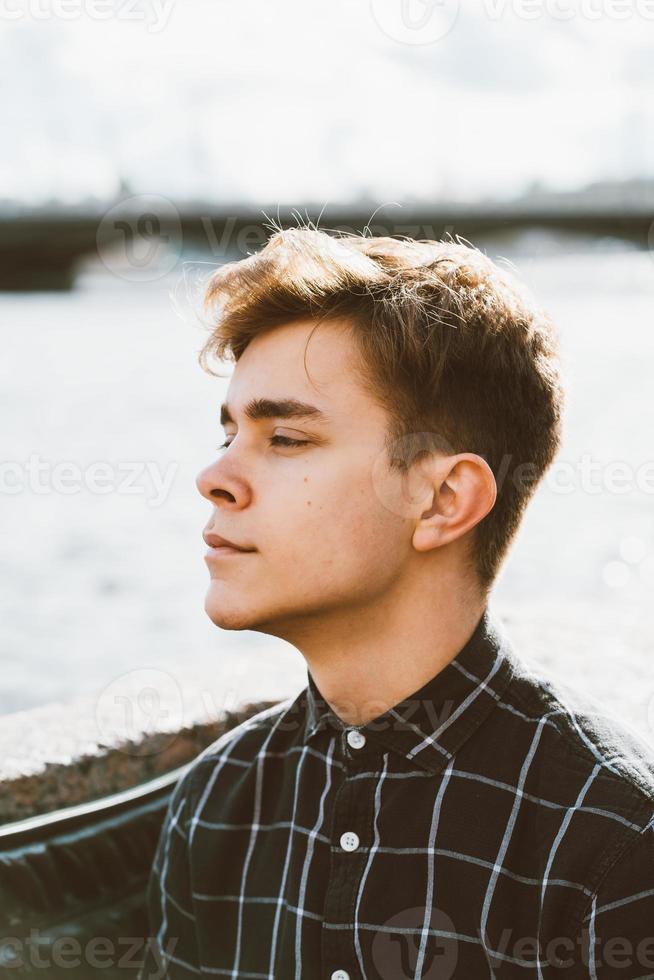 retrato de chico joven, morena con cabello oscuro, caucásico. primer plano de un chico, chico, hombre mirando más allá de la cámara. al aire libre en la ciudad por el agua foto