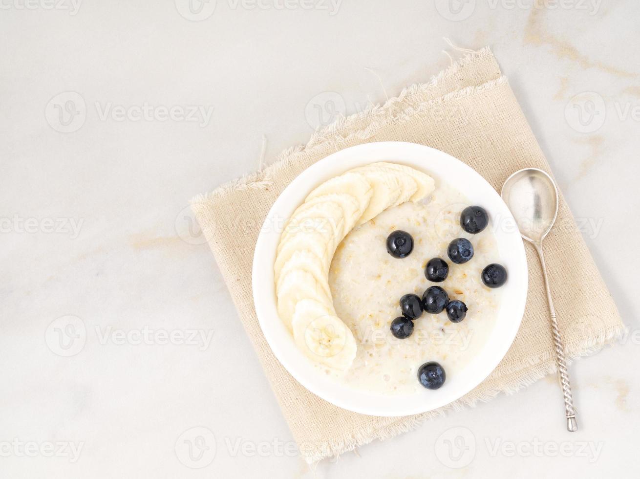 Large bowl of tasty and healthy oatmeal with fruits and berry for Breakfast, morning meal. Top view, white marble table photo