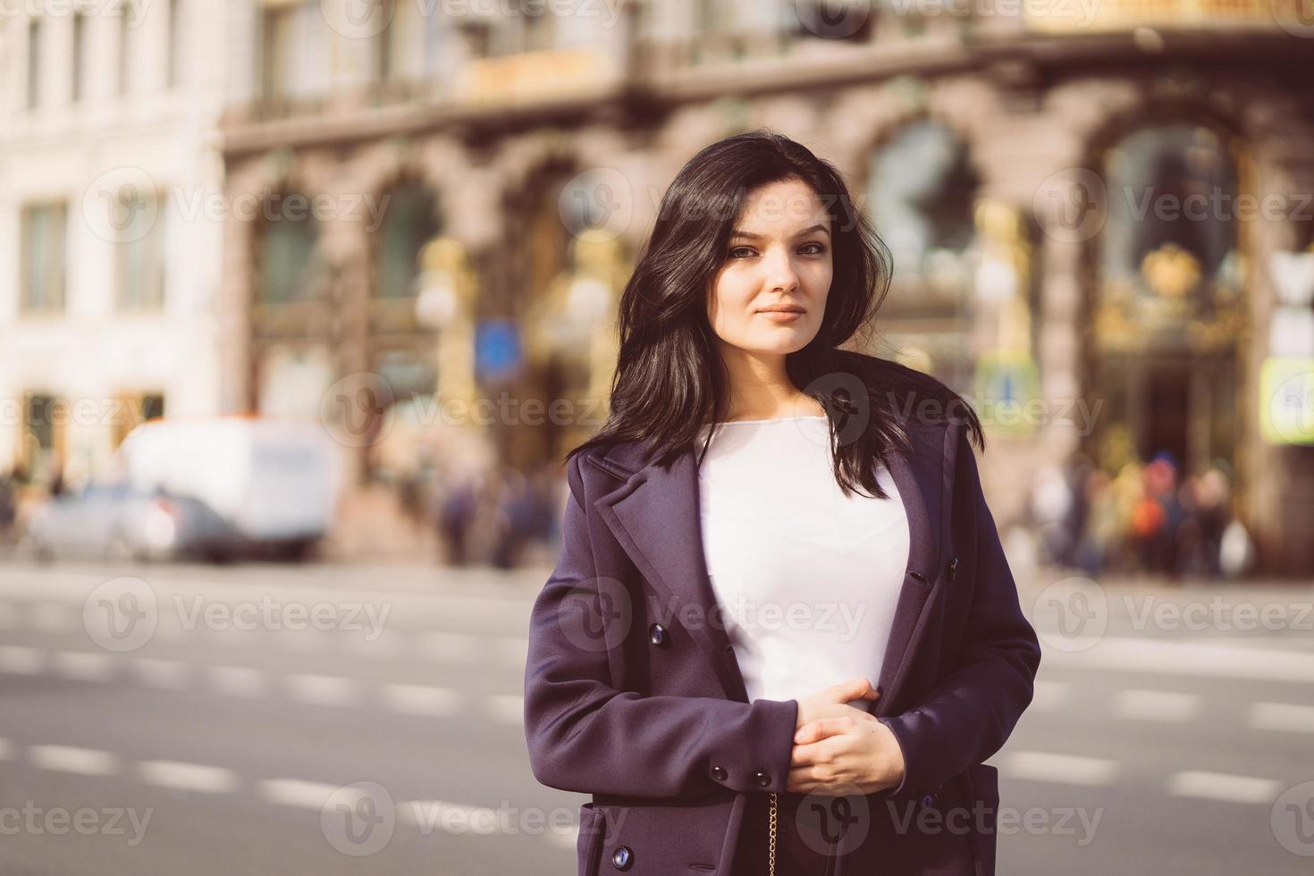 Portrait f beautiful intelligent brunette who walks down street of Saint-Petersburg in city center. Charming thoughtful woman with long dark hair wanders alone, immersed in thoughts photo