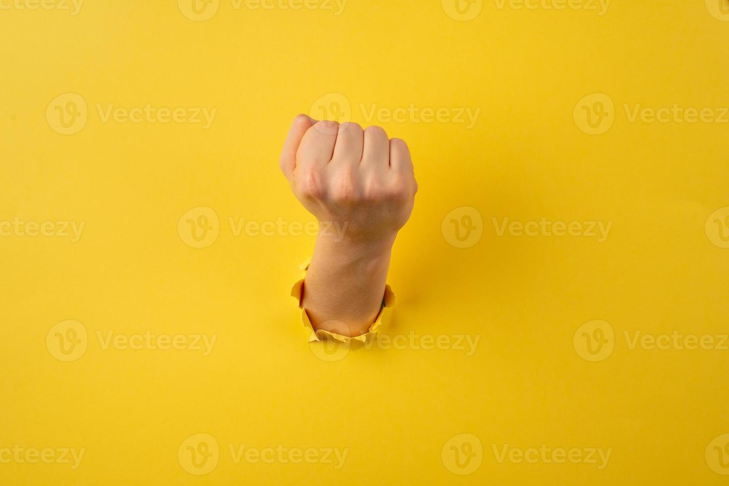 Man showing his fist from the bursted hole on orange cardboard background photo