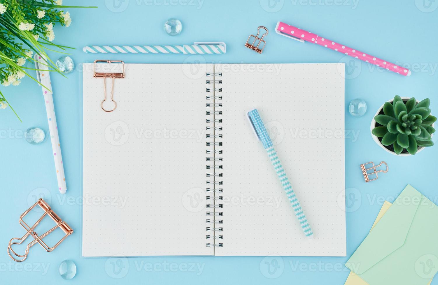 Blank notepad page in bullet journal on bright blue office desktop. Top view of modern table with notebook, stationery. Mock up, copy space, concept for diary photo