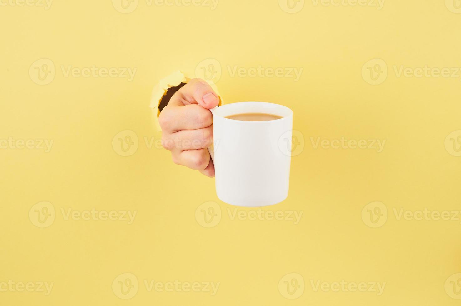 Unrecognizable person holding a cup of tea on yellow background, copy space closeup photo
