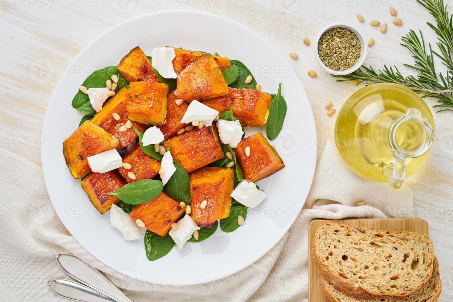 Salad with roasted pumpkin, feta cheese, spinach, nuts with honey and seasonings, top view photo