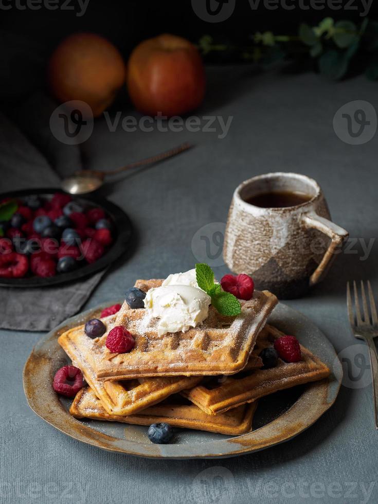 Belgian waffles with raspberries, chocolate syrup. Breakfast with tea on dark background photo