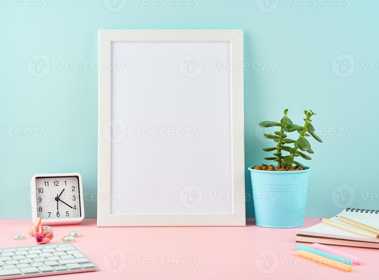 maqueta con marco blanco en blanco, alarma, bloc de notas, taza de café en mesa rosa contra pared azul foto