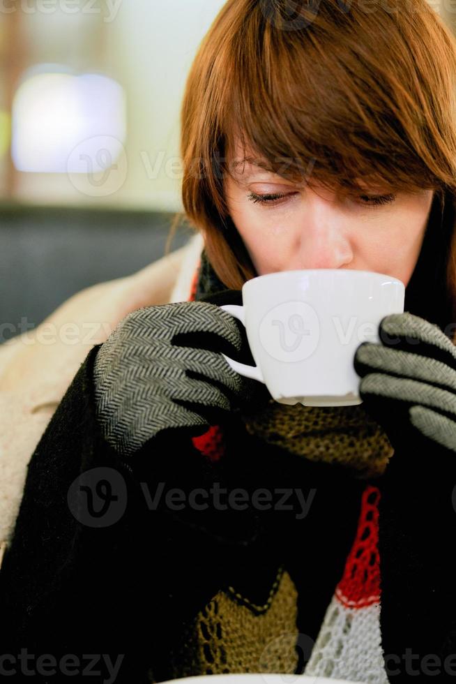 Frozen girl is warming herself with hot drink. Hands in gloves hold cup of coffee or tea photo