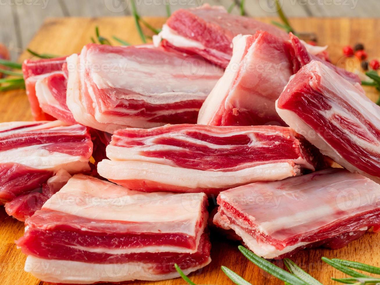 pequeños trozos de costillas de cordero crudas sobre una tabla de cortar de madera sobre un antiguo fondo rústico de madera, vista lateral foto