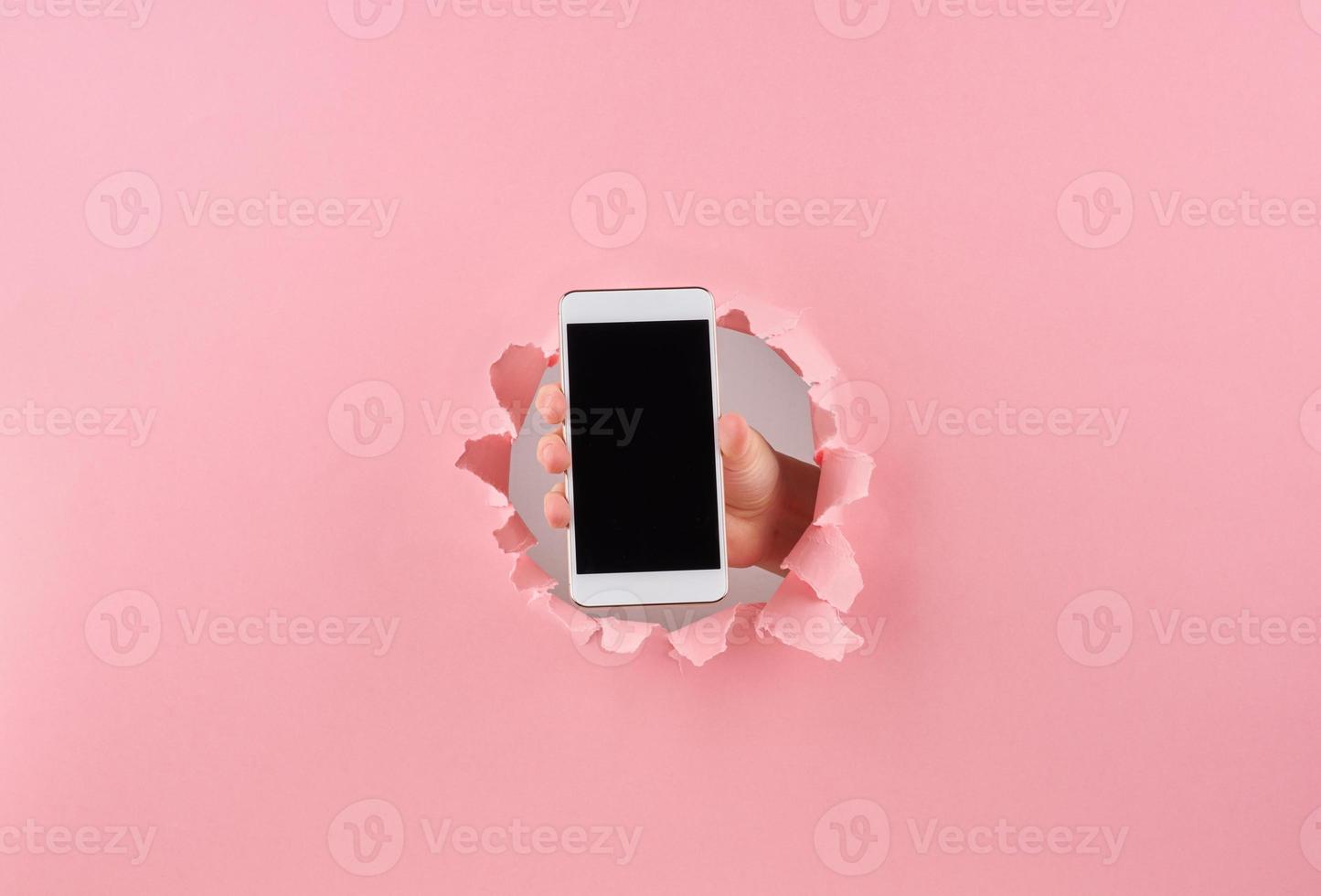 mujer sosteniendo un teléfono inteligente en un agujero envuelto en fondo rosa, espacio de copia foto