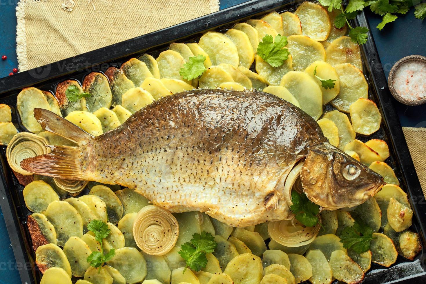 carpa al horno, pescado entero al horno con patatas en rodajas en una bandeja grande. plato tradicional polaco foto