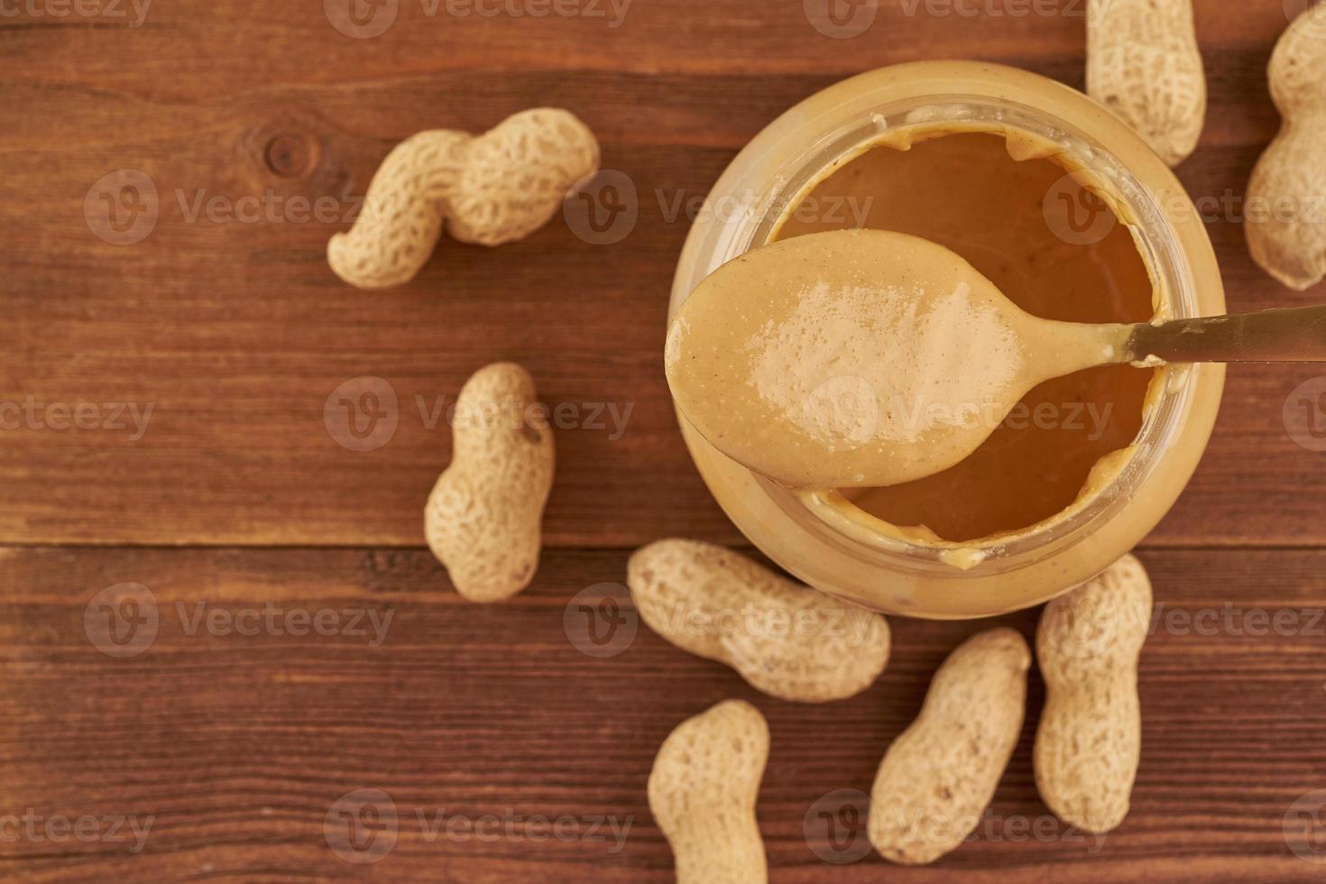 jar of peanut butter and peanuts in a shell on brown wooden table, side view, fresh crushed ground nuts, top view, copy space photo