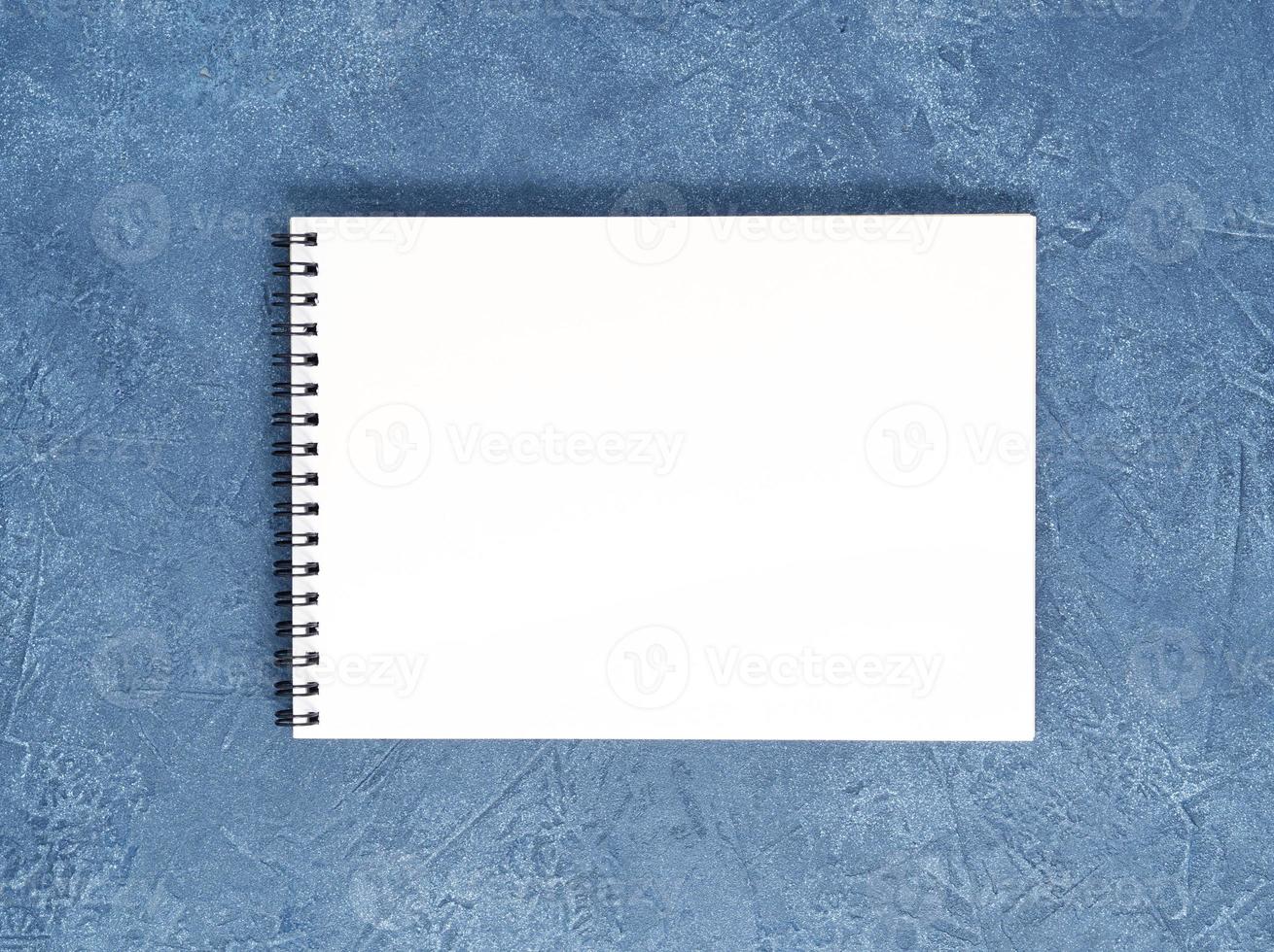 The open notepad with clean white page on aged dark blue stone table, top view photo