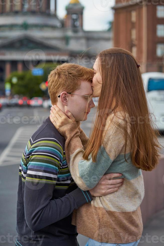 mujer pelirroja besa a un hombre en la parte superior de su cabeza, una mujer con cabello largo y oscuro y grueso en un suéter calma y consuela a un niño foto