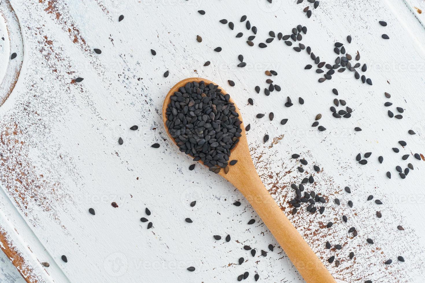 Black Sesame on wooden spoon. White wooden background. Top view, close up. Copy space. photo