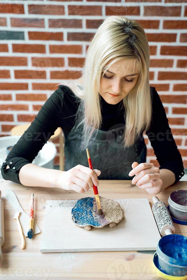 Woman making pattern on ceramic plate with paint brush. Creative hobby concept. Earn extra money, side hustle, turning hobbies into cash, passion into job, vertical photo