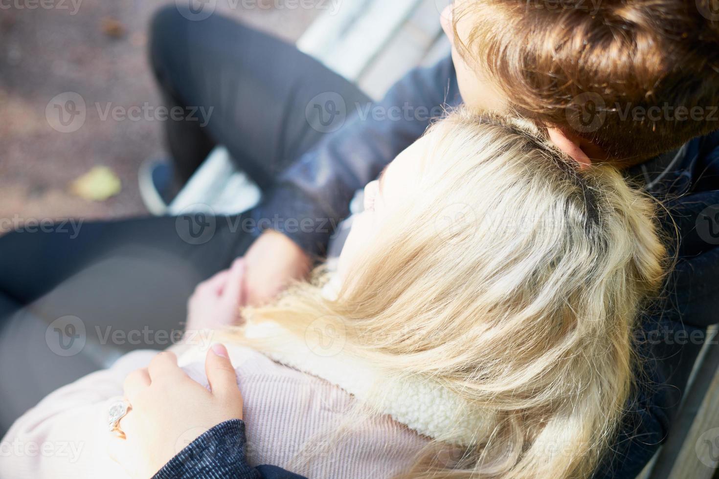 adolescentes enamorados se sientan en un banco, cabeza con cabeza, solos, en reclusión en un parque en otoño. foto