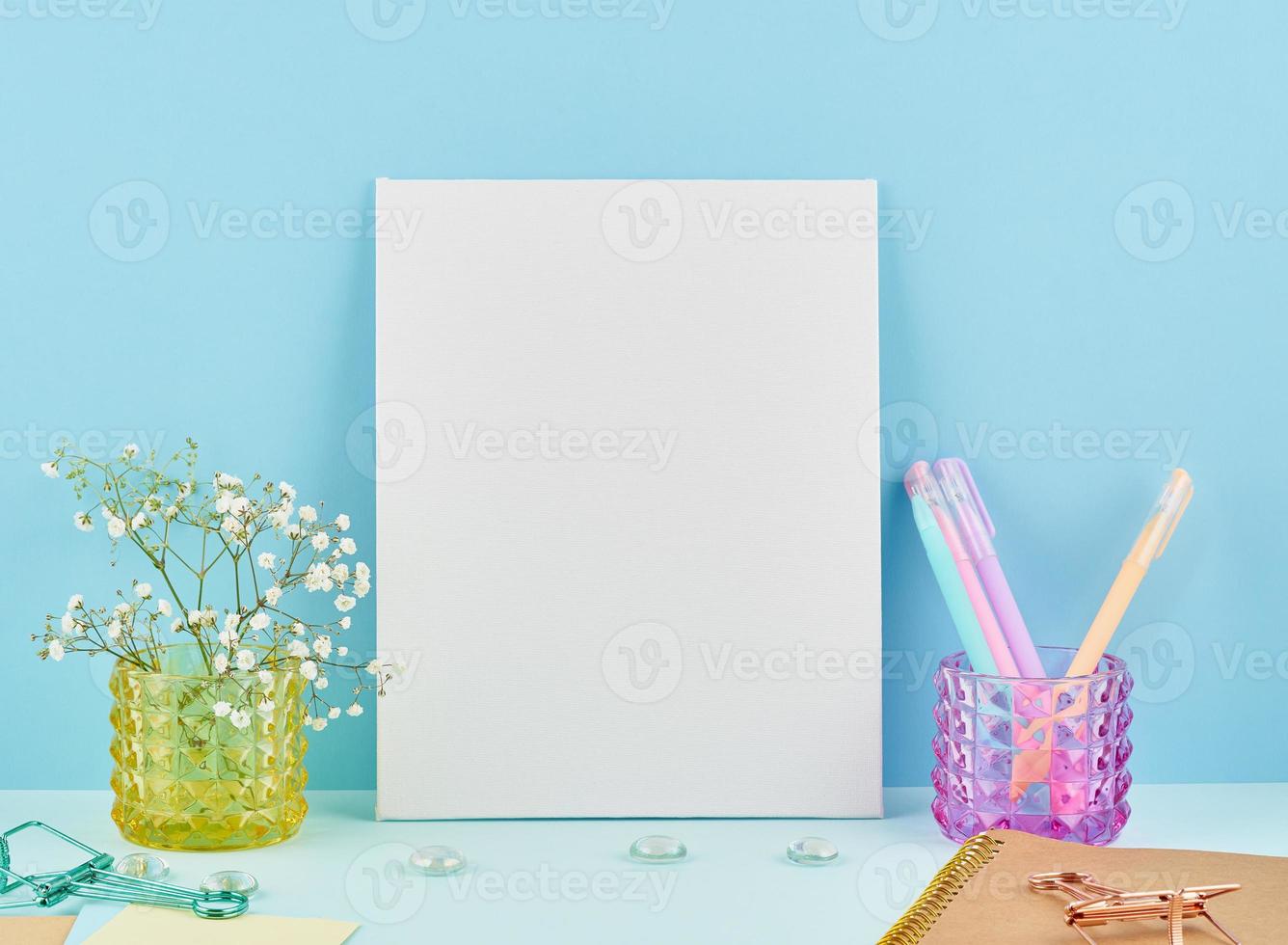 Mockup with blank white frame on blue table against blue wall, flower in vaze. photo