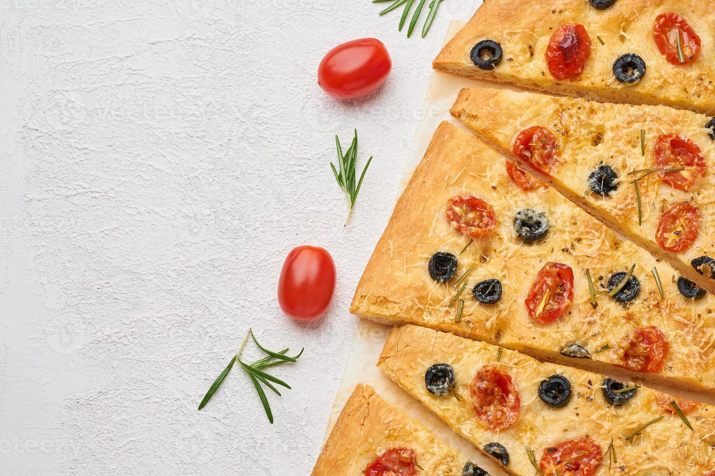Focaccia, pizza with tomatoes, olives and rosemary. Sliced Italian flat bread photo