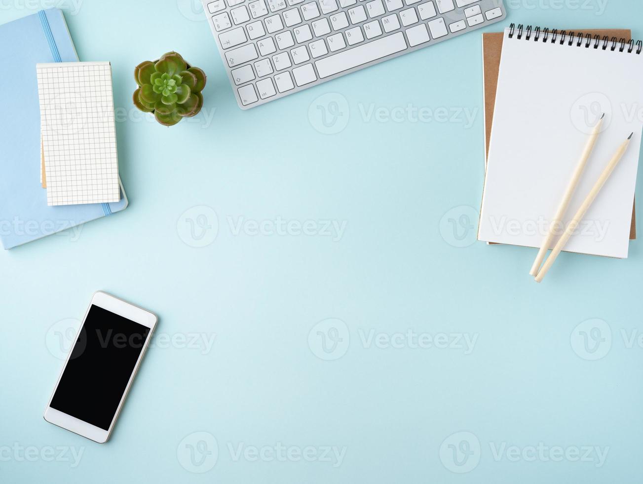 Top view of modern blue office desktop with blank notepad, computer, smartphone. Mock up photo