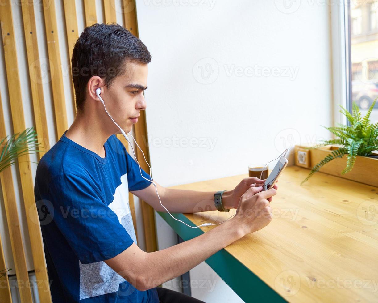 mensaje de texto para adultos jóvenes en un teléfono inteligente y escuchando música en auriculares en una cafetería foto