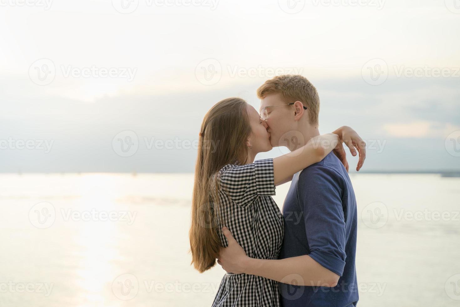 Teen couple kissing on the beach, boy and girl embracing while kissing closeup photo