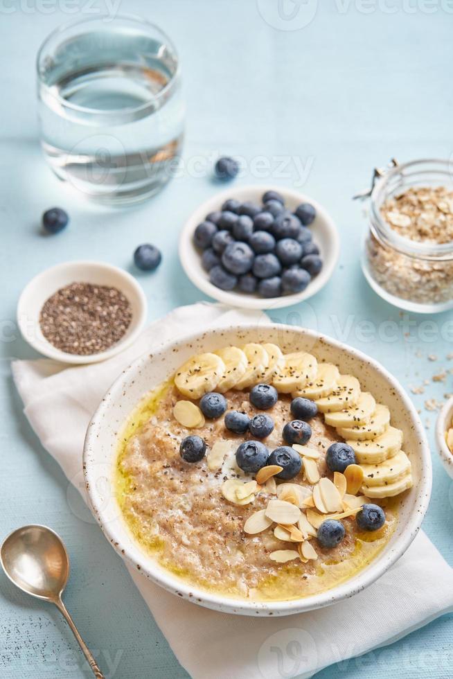 avena con arándanos, plátano y taza de agua sobre fondo azul claro. foto