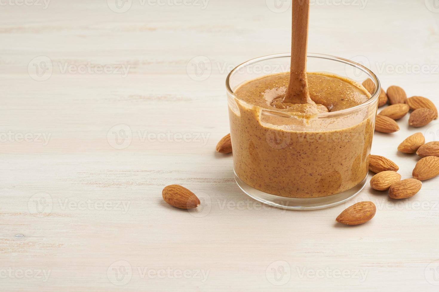 almond butter, raw food paste made from grinding almonds into nut butter, crunchy and stir, white wooden table, copy space photo