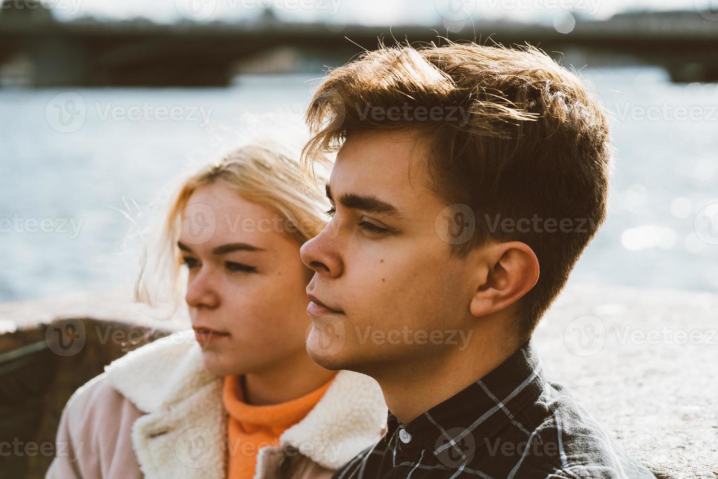 Teenagers in love sit on the waterfront in the city center, resting in autumn sun. Concept the first teenage love, the beginning of relations. A boy and a girl meet on a date, a couple. Boy closeup photo